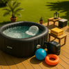 Premium inflatable hot tub on sunlit backyard deck with clear water, towels, beach ball, and lush greenery