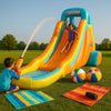 Premium inflatable water slide on green grass at sunset with splash pool, towels, and beach balls